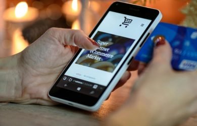 Woman using smartphone for online shopping with credit card in hand, festive background lighting.